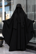 Femme portant un jilbab 2 pièces noir en crêpe royal, composé d'un khimar long et d'une jupe ample, avec les bras ouverts mettant en valeur l'ampleur et le tombé fluide du vêtement.