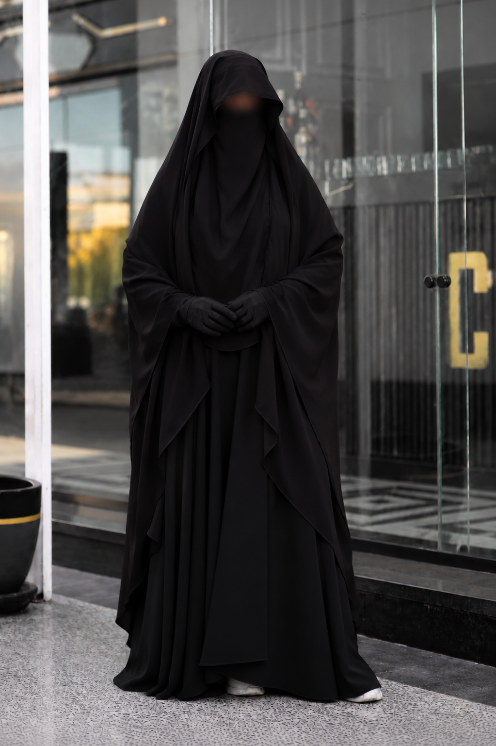 Jilbab 2 pièces noir en crêpe royal porté de face avec les mains jointes, offrant une couvrance complète, une coupe ample et un tombé élégant.