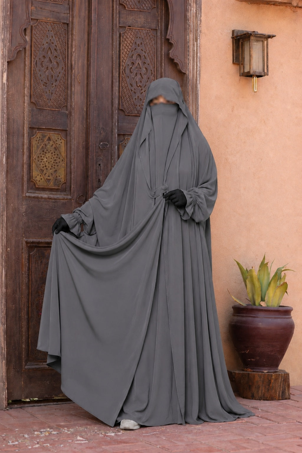 Femme portant un jilbab Liyane gris en crêpe royale, présentant l'ampleur et la fluidité du tissu avec les deux boutons à l'avant, taille unique.