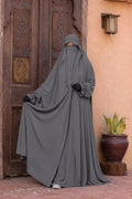 Femme portant un jilbab Liyane gris en crêpe royale, présentant l'ampleur et la fluidité du tissu avec les deux boutons à l'avant, taille unique.