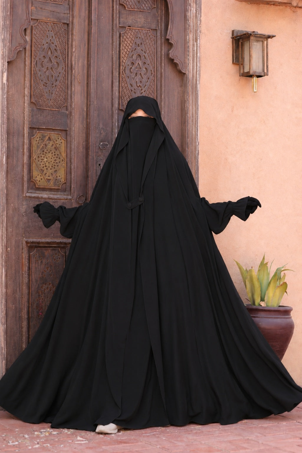 Jilbab Liyane noir à deux boutons en crêpe royale, femme présentant l'ampleur et la fluidité du tissu avec une coupe mastour élégante, manches élastiquées et taille unique adaptée aux personnes mesurant entre 1m55 et 1m75.