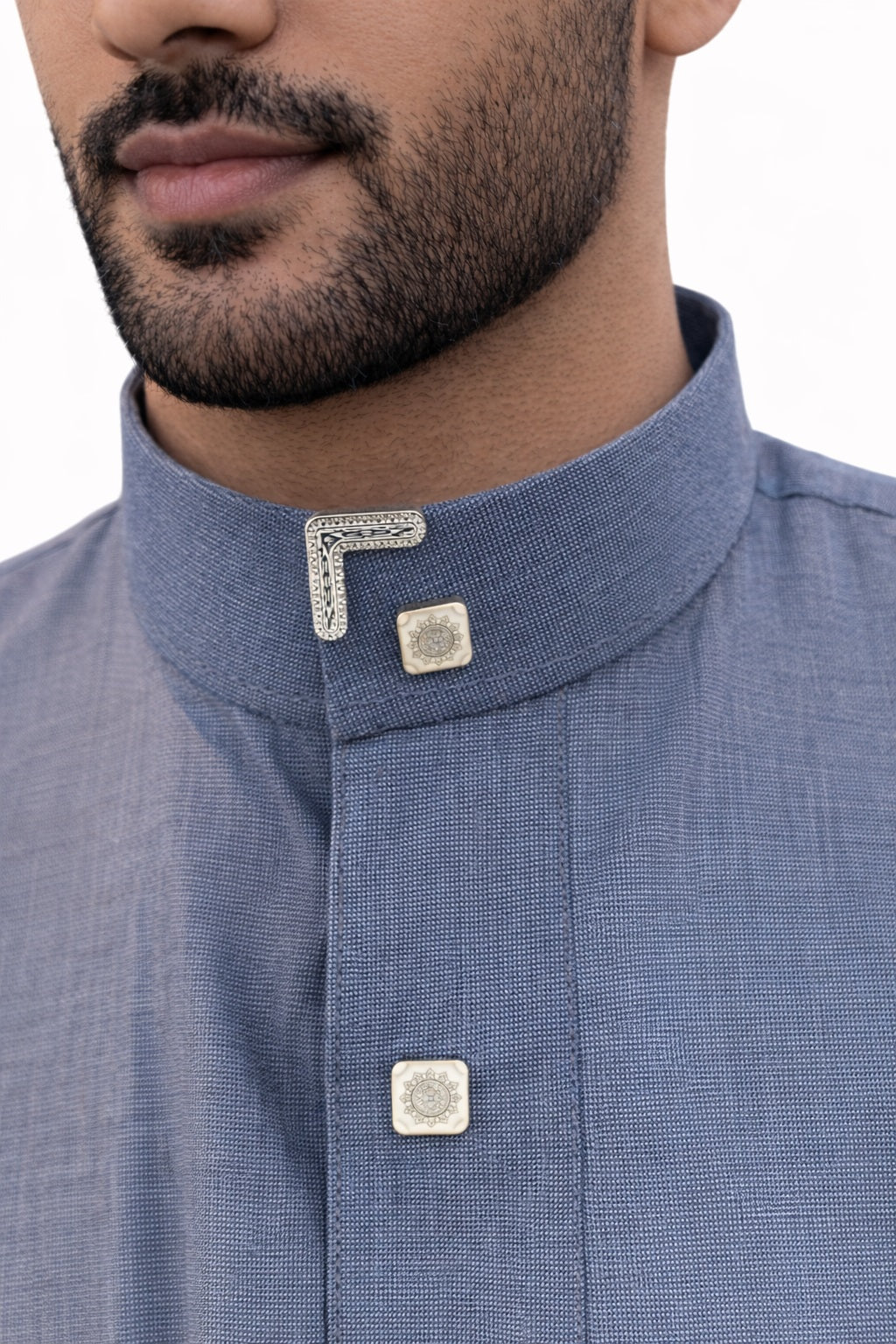 Détail du col officier d’un qamis saoudien homme bleu cendré en coton premium avec boutons carrés élégants et finitions raffinées argentées.