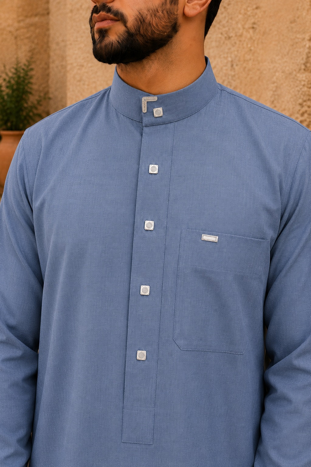 Détail du col officier d’un qamis saoudien homme bleu cendré en coton premium avec boutons carrés élégants et finitions raffinées argentées.