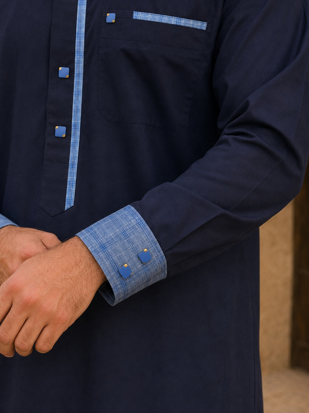 Gros plan sur la manche d'un qamis premium bleu marine avec poignets contrastés bleu ciel et double boutons carrés dorés, soulignant la qualité des finitions.