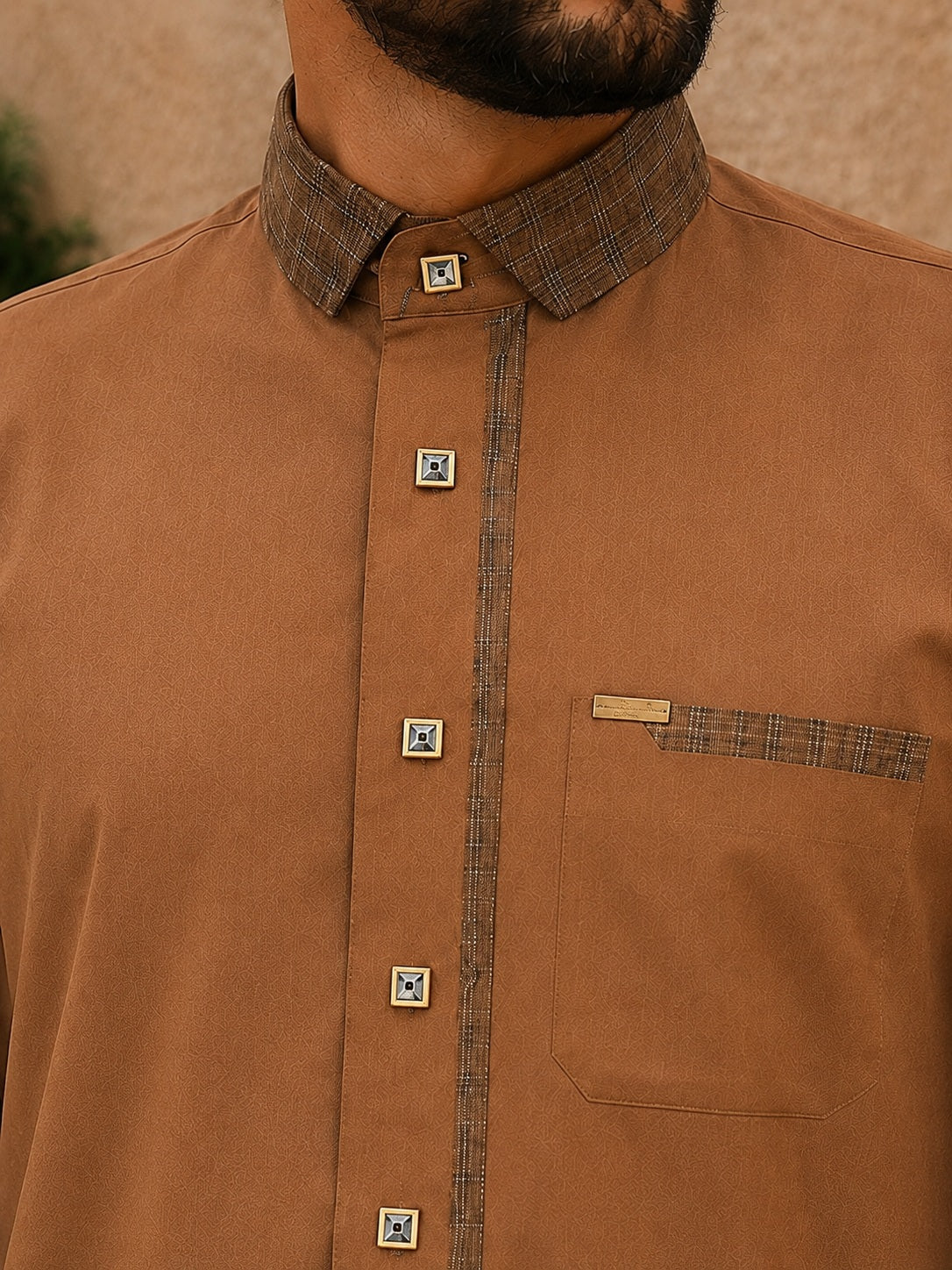 Gros plan sur le torse d'un qamis homme marron premium avec col contrasté à carreaux, boutons décoratifs dorés et poche poitrine aux finitions élégantes.