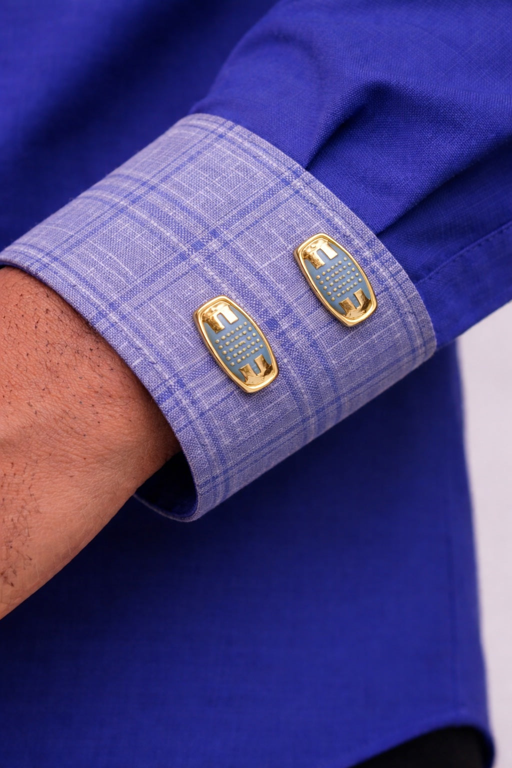 Gros plan sur la manche d'un qamis homme bleu avec poignets contrastés gris et doubles boutons dorés, finition haut de gamme.